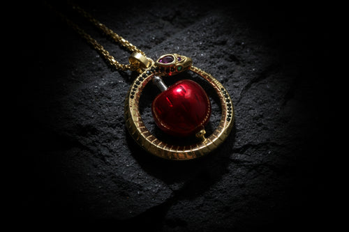 Gold pendant with a red gemstone on a dark textured background